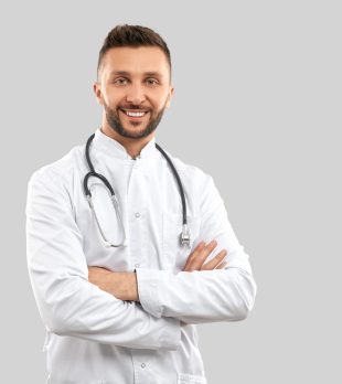 Front view of attractive confident brunette male doctor wearing lab coat and stethoscope, looking at camera with happy facial expression. Close up of intern isolated on grey. Concept of medicine.